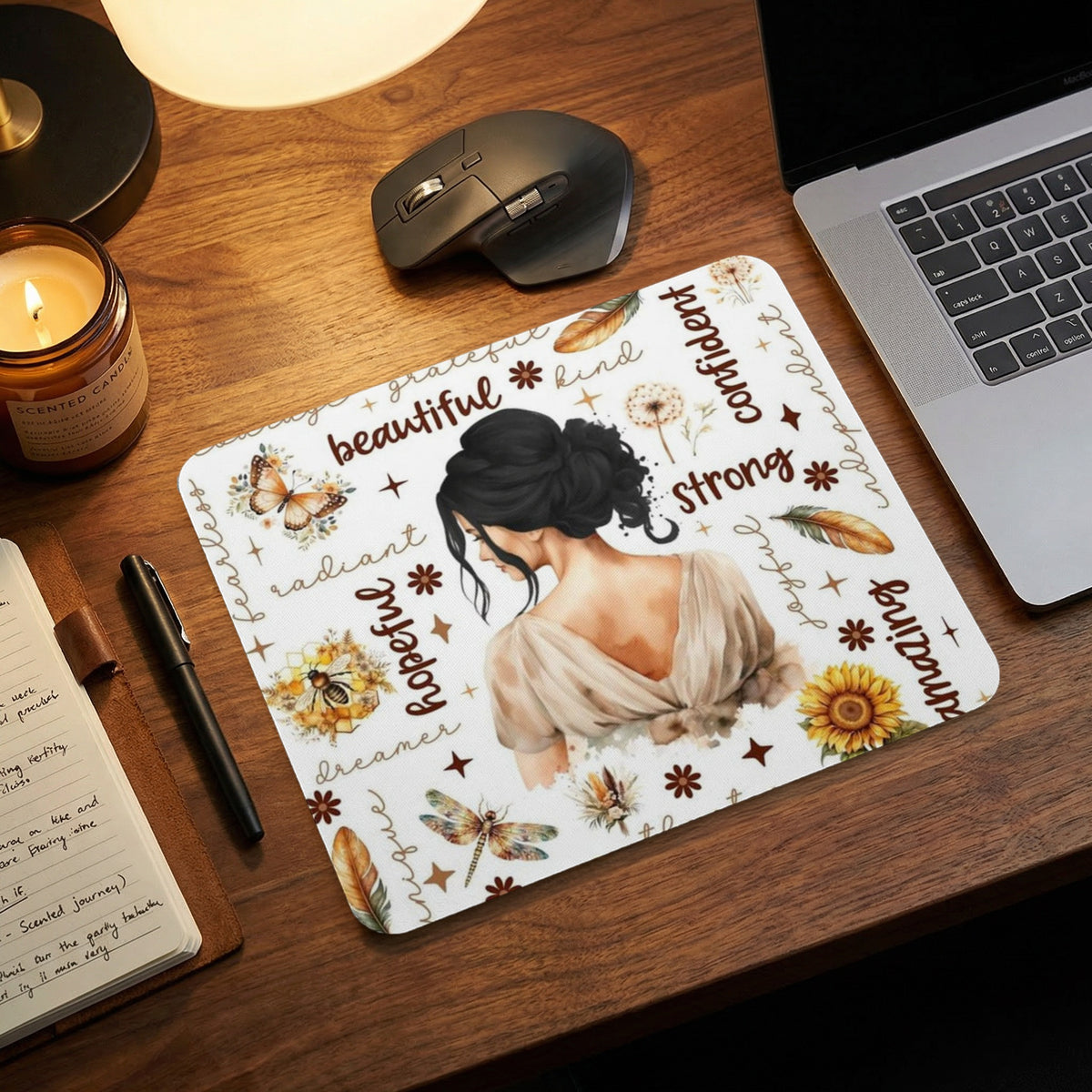 A mousepad on a wooden desk featuring an illustration of a woman surrounded by positive words.