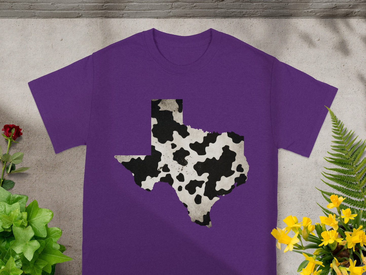 Purple t-shirt with a black and white cow print Texas outline graphic.