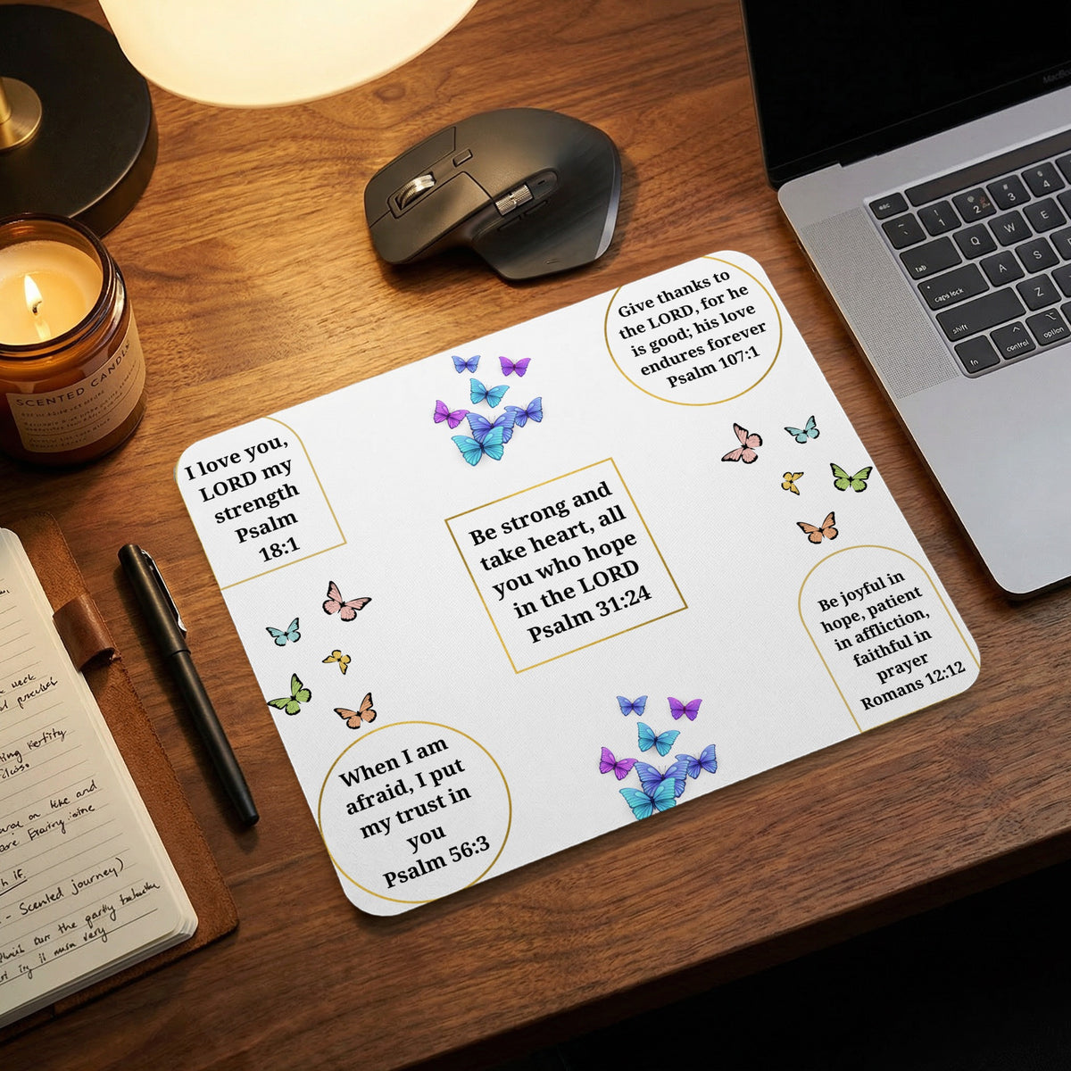 A white mousepad featuring Christian Bible verses and blue, purple, and pink butterflies on a wooden desk.