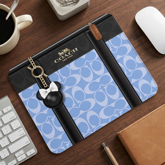 A blue and black Coach monogram laptop sleeve adorned with a mouse-ear charm.