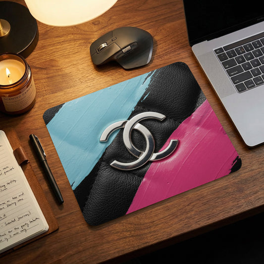 Mousepad with black leather, silver logo, and pink and blue paint strokes.