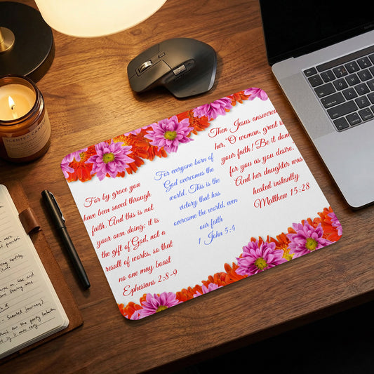 A mouse pad printed with Bible verses and floral designs lies on a wooden desk next to a laptop.