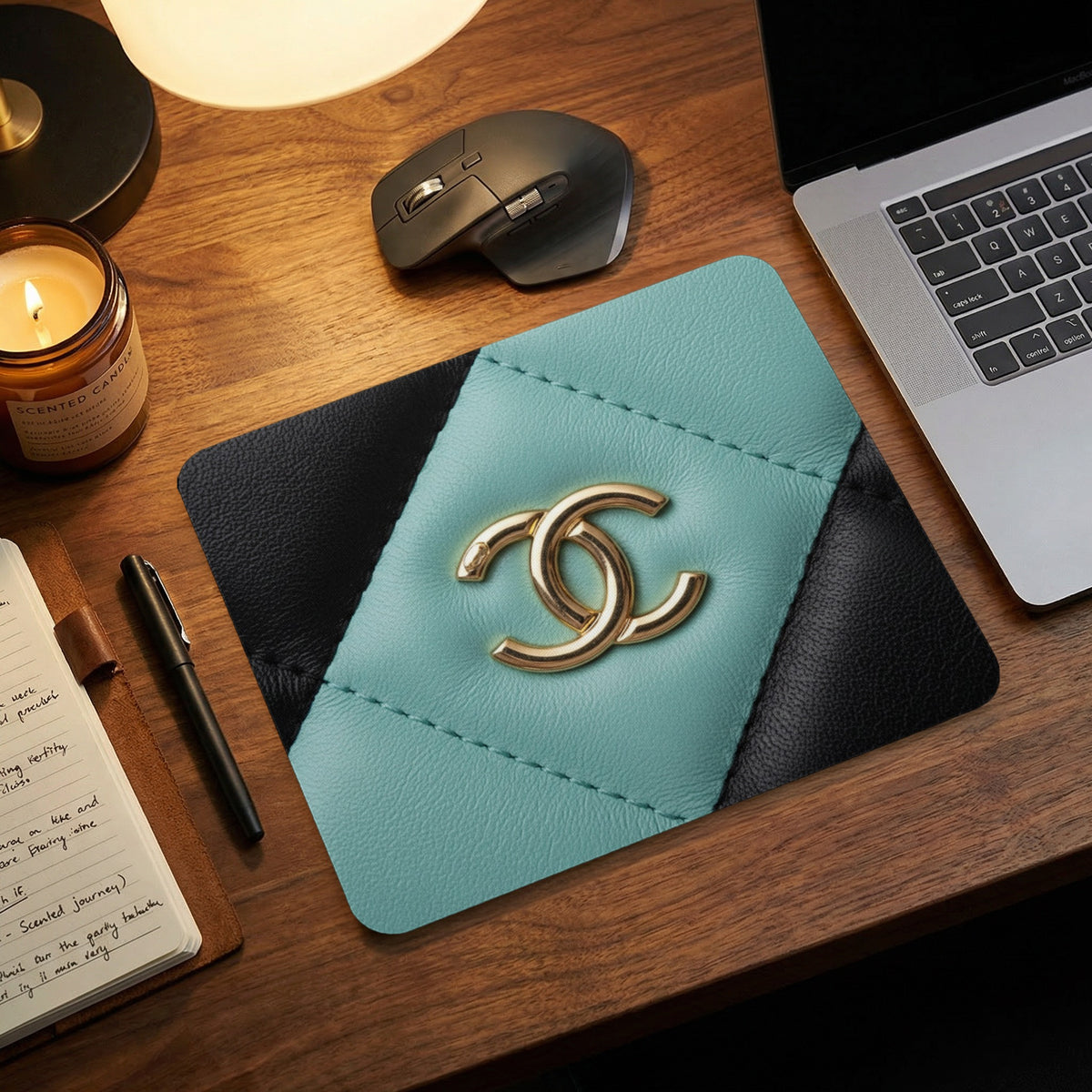 Teal and black mousepad with interlocking gold logo on a wooden desk.