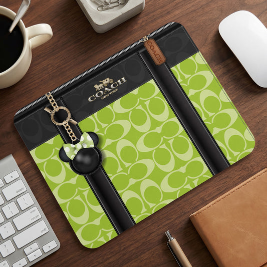 Coach bag with neon green monogram pattern and Mickey Mouse charm on desk.