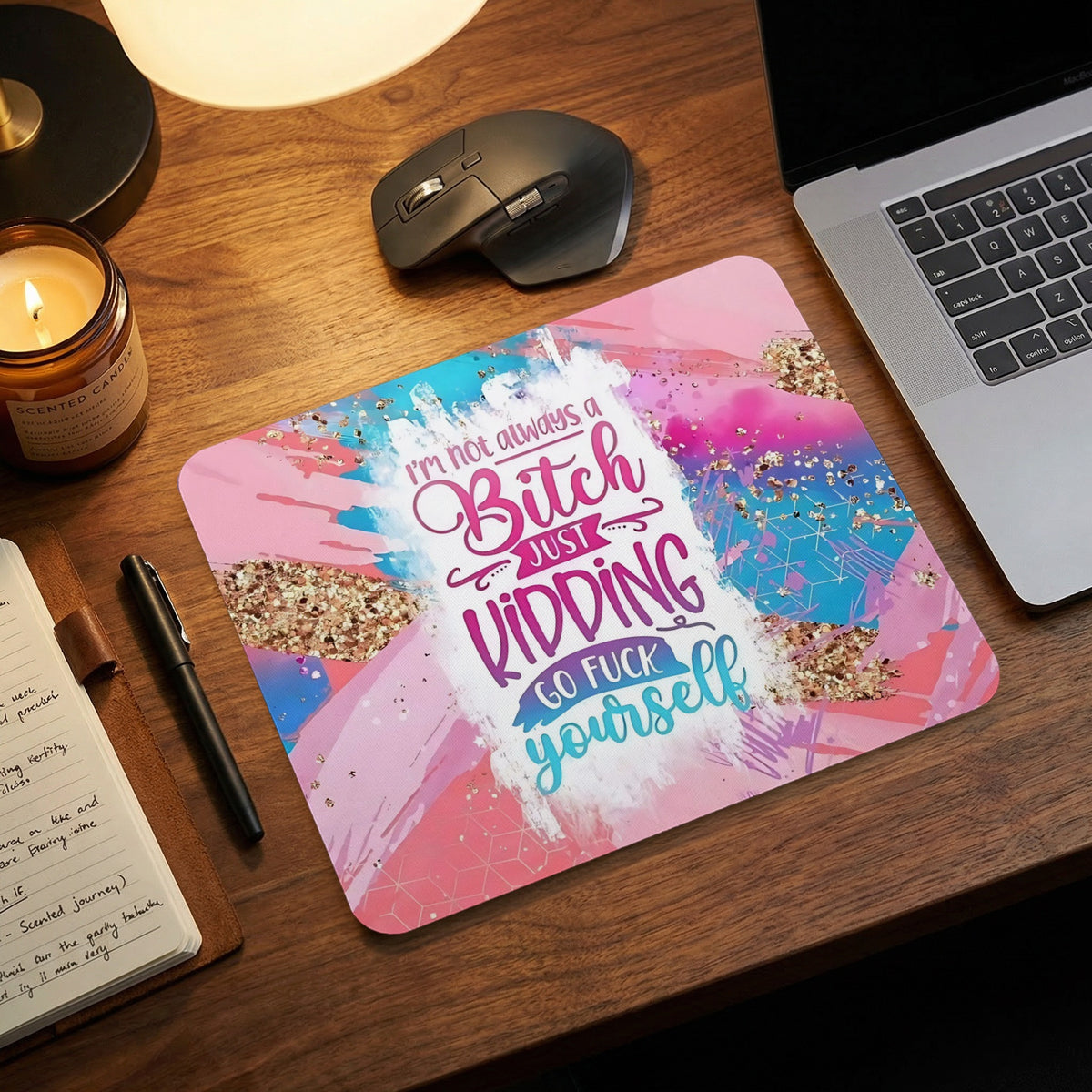 A rectangular mouse pad with abstract pink and blue watercolor background and humorous text sitting on a wooden desk.
