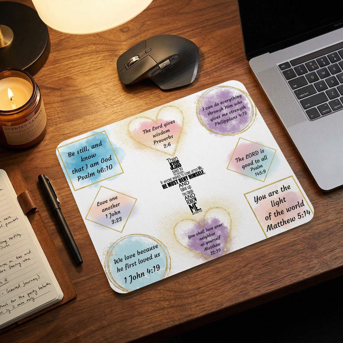 A white mousepad featuring colorful watercolor shapes and inspirational Bible verses rests on a wooden desk.