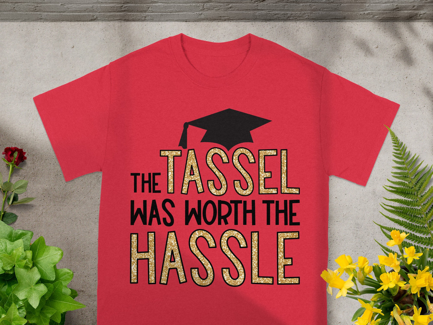 Red t-shirt with black graduation cap and gold glitter text "The Tassel Was Worth the Hassle."