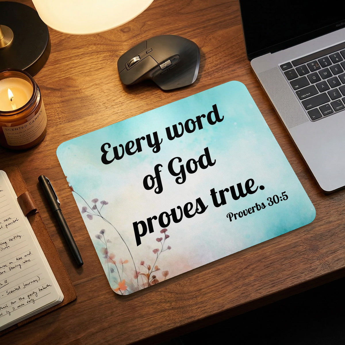 A turquoise mouse pad with black text reading Every word of God proves true Proverbs 30:5 sits on a wooden desk.
