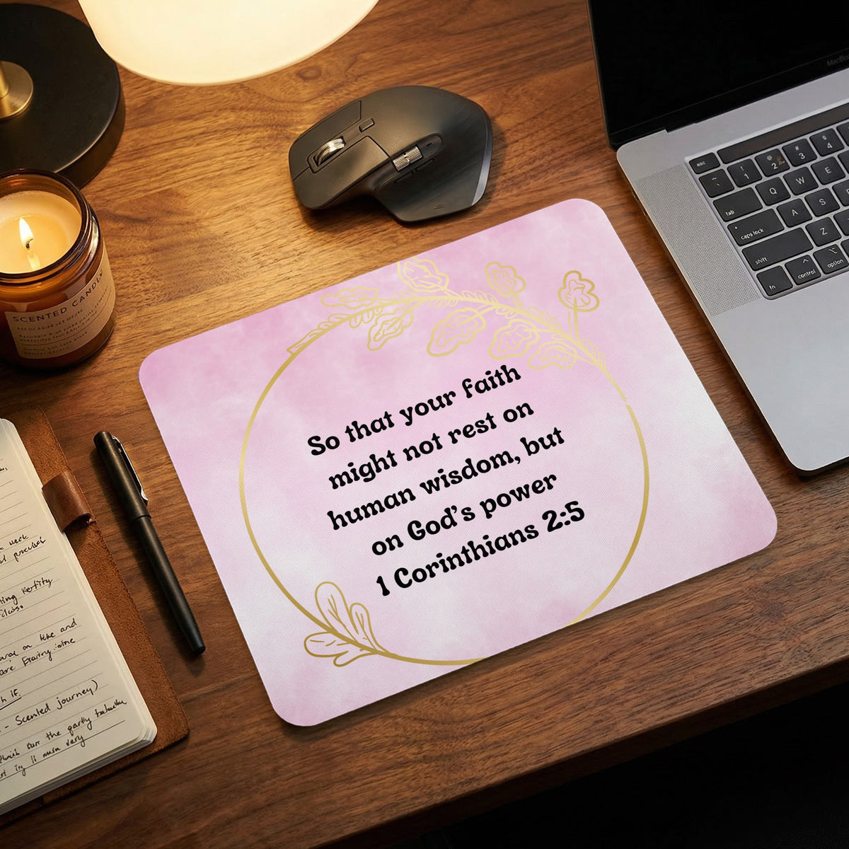 Pink rectangular mousepad with a gold leaf circle and religious quote on a wooden desk.