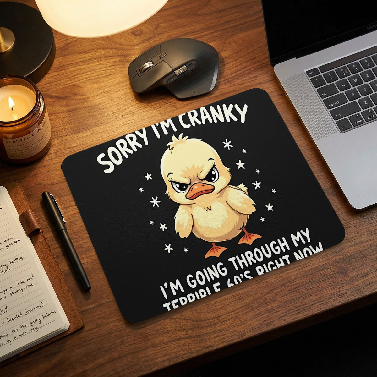 A black mousepad on a wooden desk features an angry yellow duckling and humorous text.