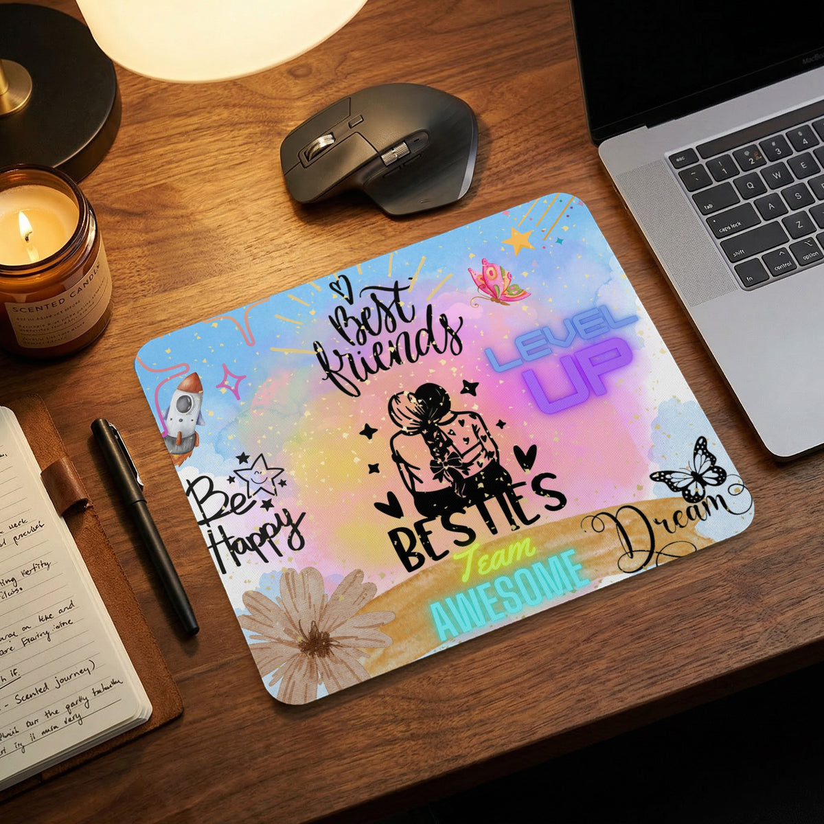 Watercolor mousepad with Best Friends and Besties text on a wooden desk near a laptop.