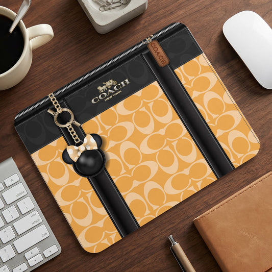 Coach patterned pouch with Mickey Mouse charm on a desk with keyboard.