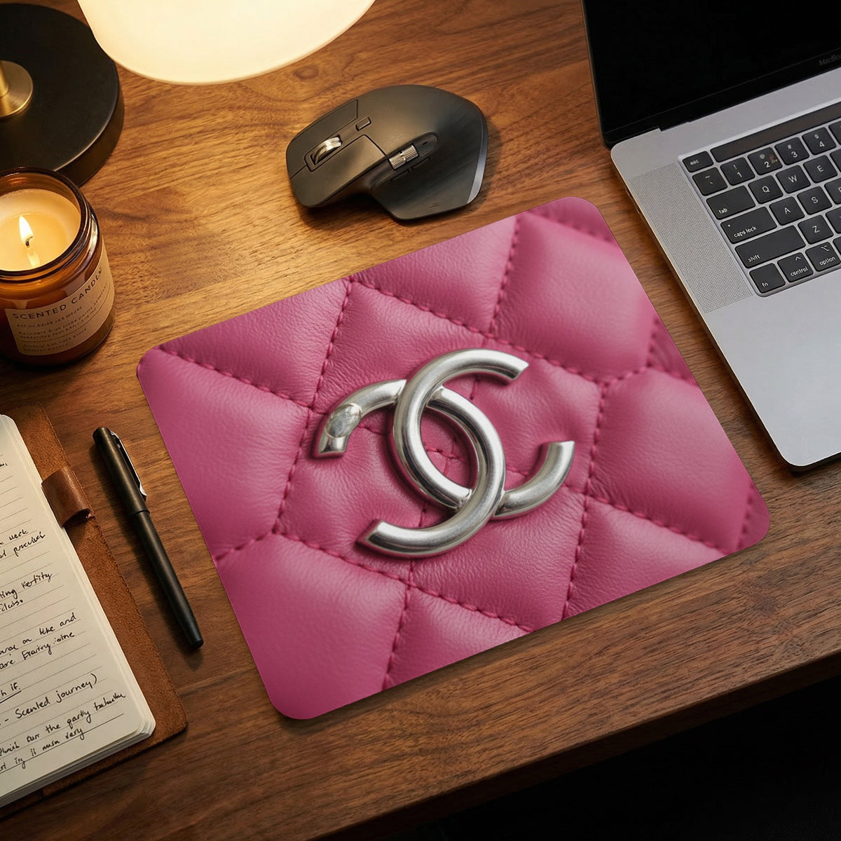 Pink quilted mousepad with silver interlocking double C logo on wooden desk.