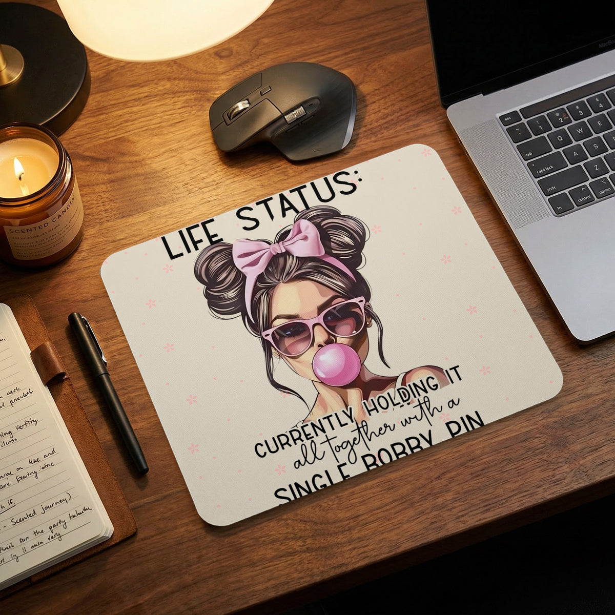 A mousepad featuring an illustration of a woman blowing a bubble, with the text Life Status: Currently holding it all together with a single bobby pin.